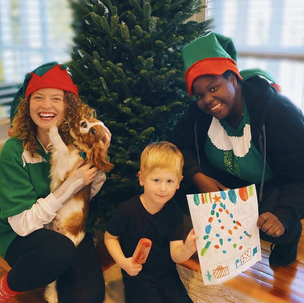 The elves, a boy holding a pop and a spaniel in front of a Fraser fir