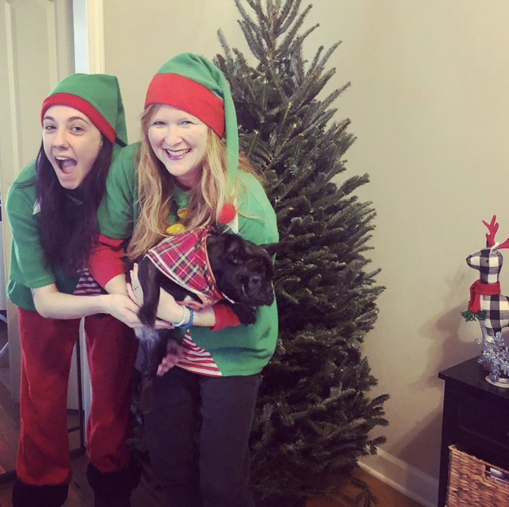 Two elves and a puppy in front of a full Fraser fir