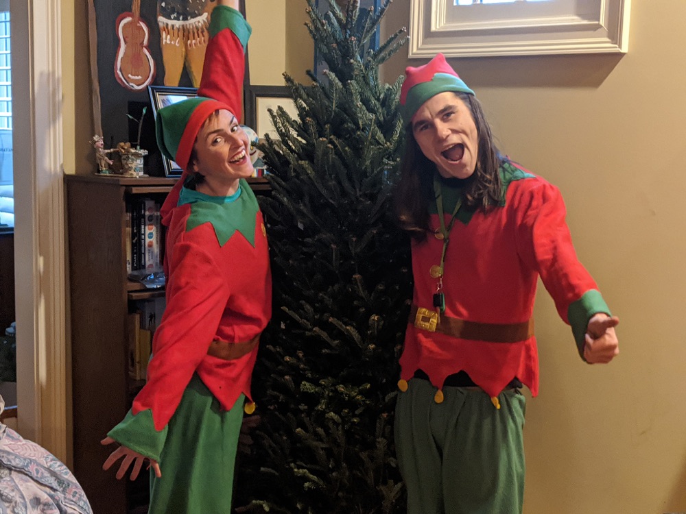 Two elves posing either side of a Fraser fir in a living room