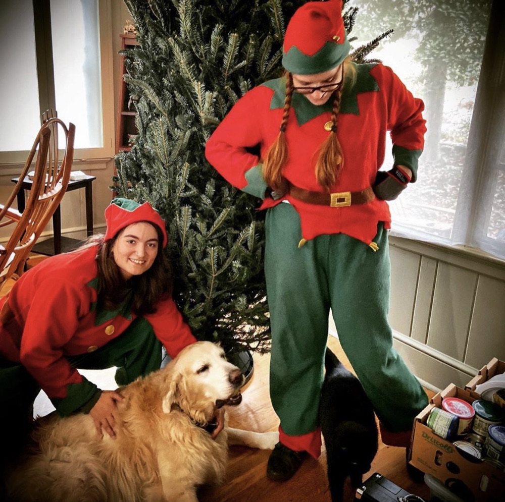 Two elves and a golden retriever in front of a tall Fraser fir