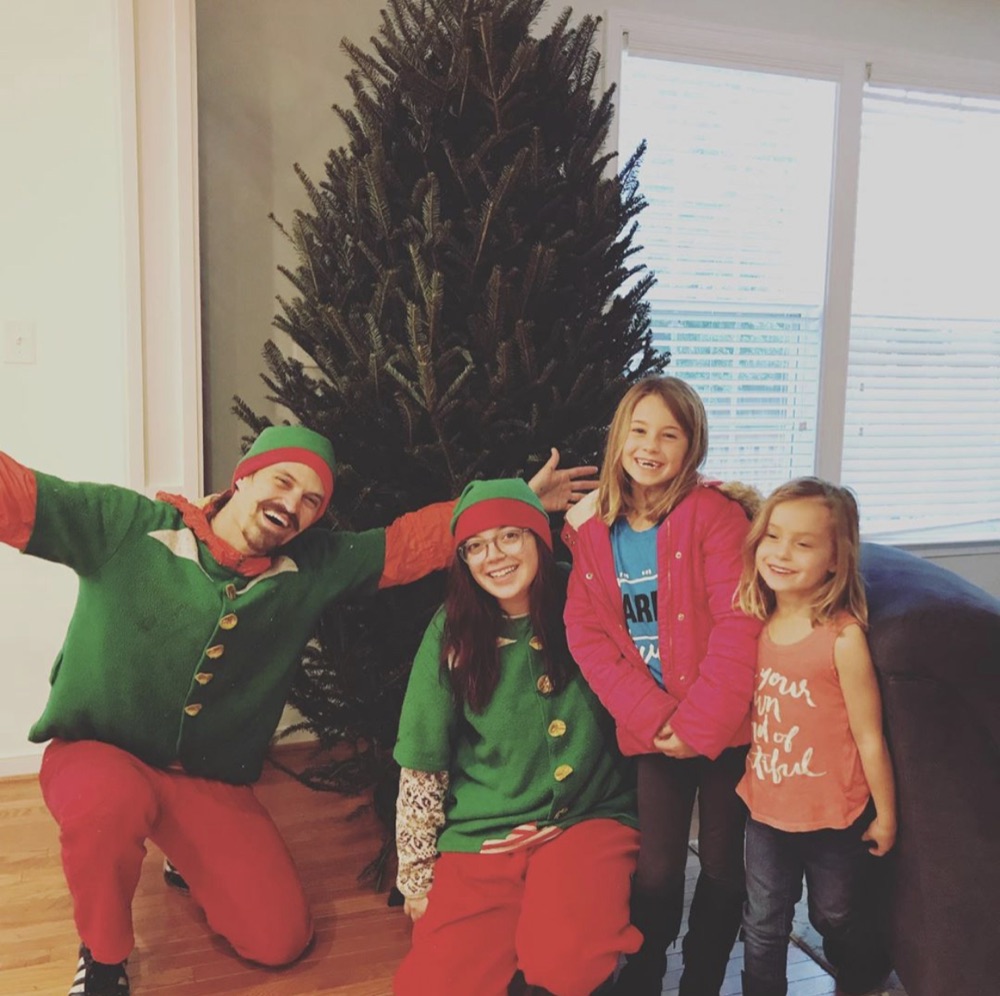 A tall Fraser fir by a window, with the elves and two girls